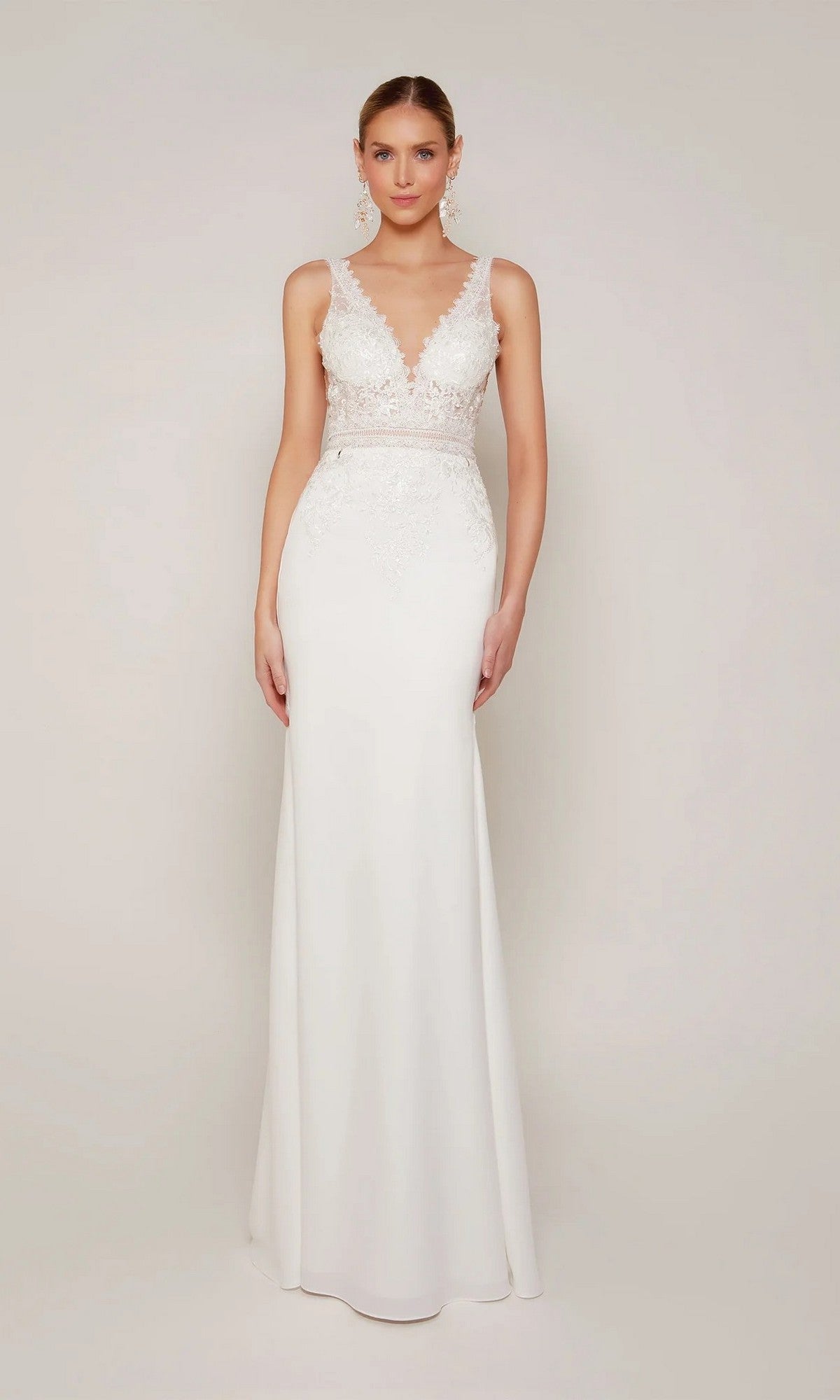 A woman stands facing forward in the Alyce 7097 long formal dress—a sleeveless white lace gown with a sheath silhouette, fitted bodice, and V-neckline—against a plain background.